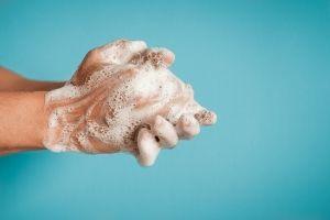 Blue background, two hands covered in soap suds in the processing of washing